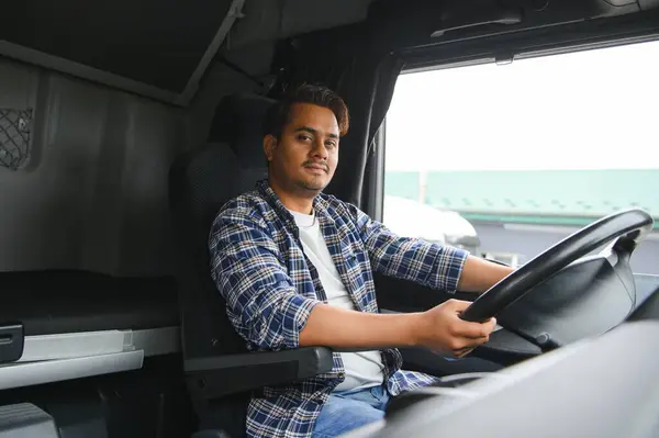 A young Indian male truck driver sits behind the wheel.