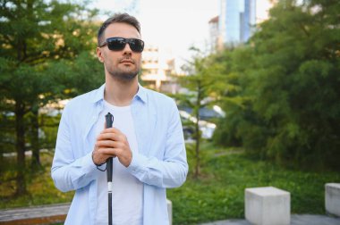 Şehirde sokakta yürüyen beyaz bastonlu genç kör adam.