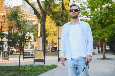 Genç, yakışıklı, kör adam kasabada sopayla yürüyor..