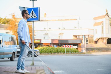 Şehirde sokakta yürüyen beyaz bastonlu genç kör adam.