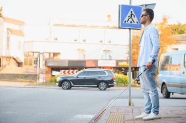 Genç, yakışıklı, kör adam kasabada sopayla yürüyor..
