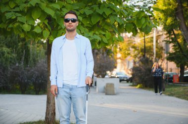 Genç, yakışıklı, kör adam kasabada sopayla yürüyor..
