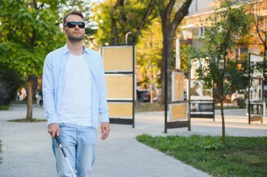 Genç, yakışıklı, kör adam kasabada sopayla yürüyor..