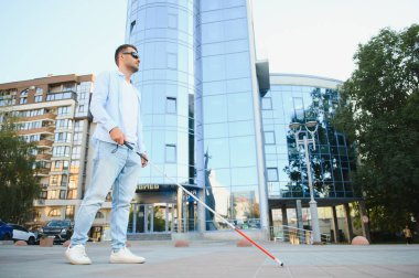 Genç, yakışıklı, kör adam kasabada sopayla yürüyor..