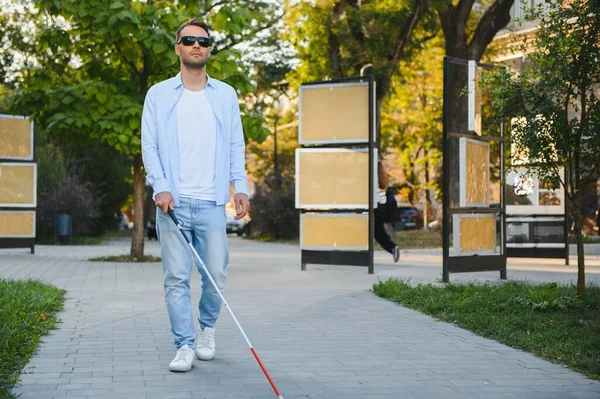 Genç, yakışıklı, kör adam kasabada sopayla yürüyor..