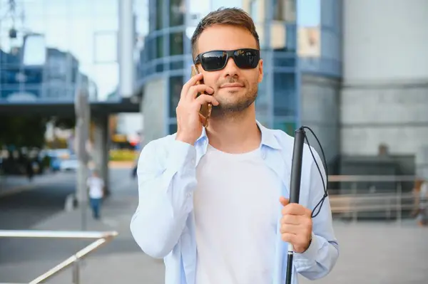 Young blind man with smartphone in city, calling.