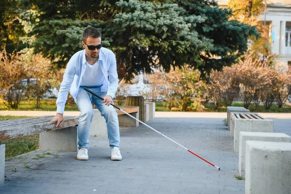 stock image Blind man with a walking stick sitting on a bench at a park.