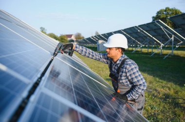 Mavi gökyüzüne karşı güneş panellerinin yanında duran beyaz şapkalı genç Hintli teknisyen portresi. Endüstriyel işçi güneş sistemi kurulumu, yenilenebilir yeşil enerji üretimi kavramı