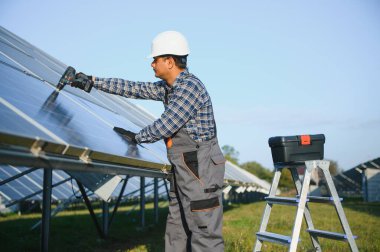 Kasklı ve kahverengi tulumlu erkek Arap mühendis güneş panellerindeki direnci kontrol ediyor. İstasyonda çalışan Hintli adam..