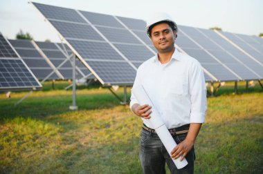 Genç Hintli teknisyen ya da yönetici güneş panelinin yanında duran resmi giysiler giyiyor. Yenilenebilir enerji, çapraz duran adam, boşluğu kopyala.