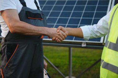 İş adamı ve mühendisler inşaat halindeki evlere güneş panelleri kurmayı tartıştıktan sonra el sıkışıyor, konut için yenilenebilir enerji.