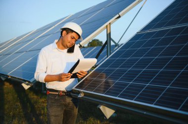 Genç Hintli teknisyen ya da yönetici güneş panelinin yanında duran resmi giysiler giyiyor. Yenilenebilir enerji, çapraz duran adam, boşluğu kopyala.