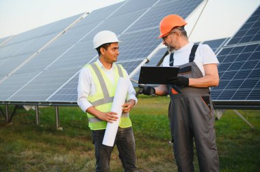 Şu anda yenilenebilir güneş enerjisi santrallerine güneş panelleri kurma planları üzerinde çalışan iki erkek mühendis. Mühendis ekibi kırsal bölgelere güneş pilleri kurmaktan bahsediyor..
