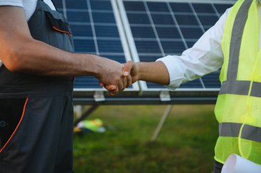 Workers shaking hands on a background of solar panels on solar power plant.