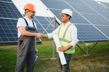Şu anda yenilenebilir güneş enerjisi santrallerine güneş panelleri kurma planları üzerinde çalışan iki erkek mühendis. Mühendis ekibi kırsal bölgelere güneş pilleri kurmaktan bahsediyor..