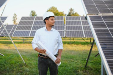Genç Hintli erkek mühendisin portresi güneş panellerinin yanında duruyor, açık mavi gökyüzü arka planı, yenilenebilir ve temiz enerjisi var. beceri Hindistan, kopyalama alanı.