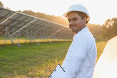 Genç Hintli erkek mühendisin portresi güneş panellerinin yanında duruyor, açık mavi gökyüzü arka planı, yenilenebilir ve temiz enerjisi var. beceri Hindistan, kopyalama alanı.