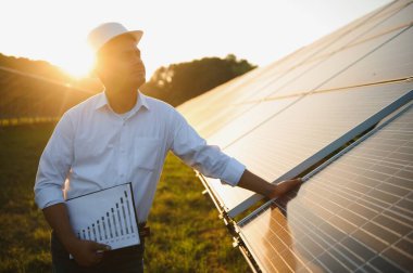 Genç Hintli erkek mühendisin portresi güneş panellerinin yanında duruyor, açık mavi gökyüzü arka planı, yenilenebilir ve temiz enerjisi var. beceri Hindistan, kopyalama alanı.