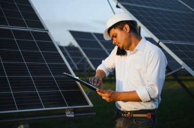 Genç Hintli teknisyen ya da yönetici güneş panelinin yanında duran resmi giysiler giyiyor. Yenilenebilir enerji, çapraz duran adam, boşluğu kopyala.