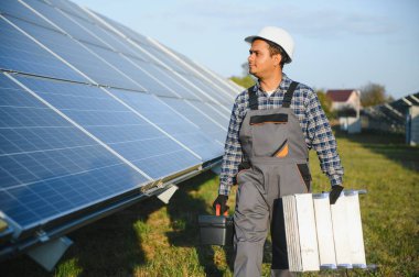 Kasklı ve kahverengi tulumlu erkek Arap mühendis güneş panellerindeki direnci kontrol ediyor. İstasyonda çalışan Hintli adam..