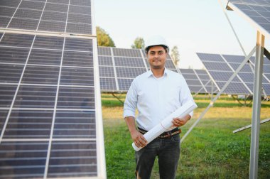 Genç Hintli teknisyen ya da yönetici güneş panelinin yanında duran resmi giysiler giyiyor. Yenilenebilir enerji, çapraz duran adam, boşluğu kopyala.