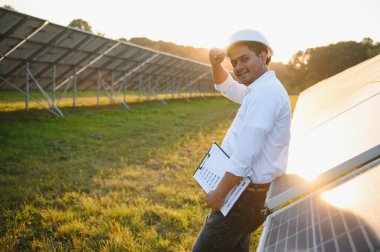 Genç Hintli teknisyen ya da yönetici güneş panelinin yanında duran resmi giysiler giyiyor. Yenilenebilir enerji, çapraz duran adam, boşluğu kopyala.