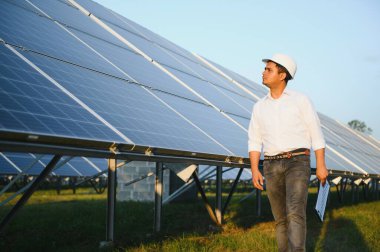 Genç Hintli erkek mühendisin portresi güneş panellerinin yanında duruyor, açık mavi gökyüzü arka planı, yenilenebilir ve temiz enerjisi var. beceri Hindistan, kopyalama alanı.