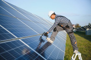 Mavi gökyüzüne karşı güneş panellerinin yanında duran beyaz şapkalı genç Hintli teknisyen portresi. Endüstriyel işçi güneş sistemi kurulumu, yenilenebilir yeşil enerji üretimi kavramı