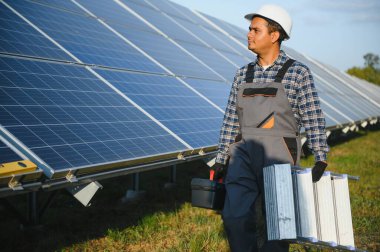 Mavi gökyüzüne karşı güneş panellerinin yanında duran beyaz şapkalı genç Hintli teknisyen portresi. Endüstriyel işçi güneş sistemi kurulumu, yenilenebilir yeşil enerji üretimi kavramı