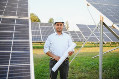 Genç Hintli erkek mühendisin portresi güneş panellerinin yanında duruyor, açık mavi gökyüzü arka planı, yenilenebilir ve temiz enerjisi var. beceri Hindistan, kopyalama alanı.