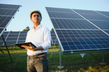 Genç Hintli teknisyen ya da yönetici güneş panelinin yanında duran resmi giysiler giyiyor. Yenilenebilir enerji, çapraz duran adam, boşluğu kopyala.