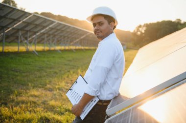 Genç Hintli teknisyen ya da yönetici güneş panelinin yanında duran resmi giysiler giyiyor. Yenilenebilir enerji, çapraz duran adam, boşluğu kopyala.