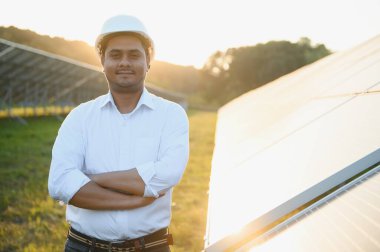 Genç Hintli teknisyen ya da yönetici güneş panelinin yanında duran resmi giysiler giyiyor. Yenilenebilir enerji, çapraz duran adam, boşluğu kopyala.