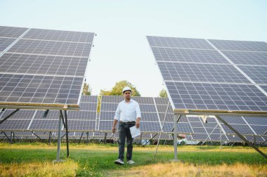 Genç Hintli erkek mühendisin portresi güneş panellerinin yanında duruyor, açık mavi gökyüzü arka planı, yenilenebilir ve temiz enerjisi var. beceri Hindistan, kopyalama alanı.