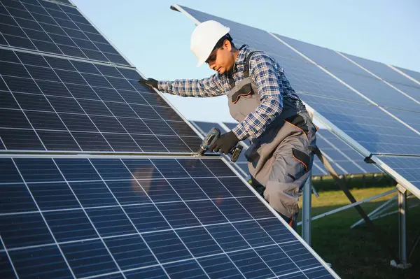 An Indian worker in uniform and with tools works on a solar panel farm.