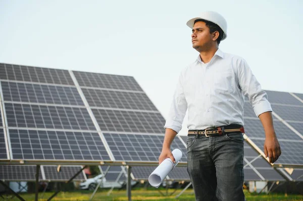 An Indian male engineer working on a field of solar panels. The concept of renewable energy.