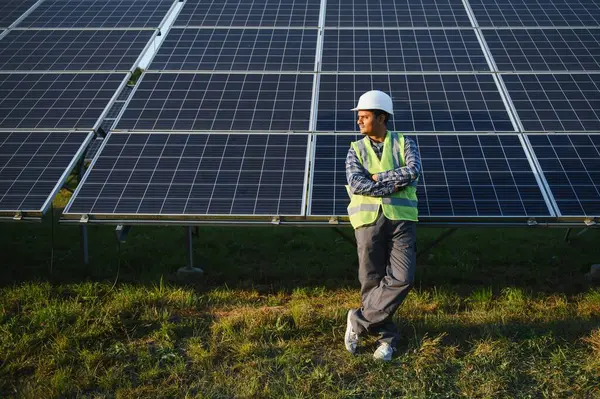 Indian man in uniform on solar farm. Competent energy engineer controlling work of photovoltaic cells.