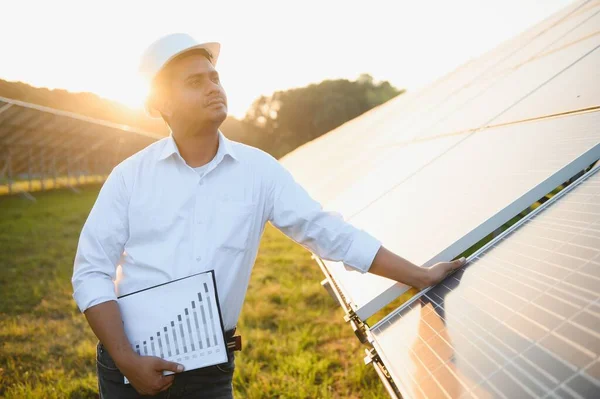 An Indian male engineer working on a field of solar panels. The concept of renewable energy.