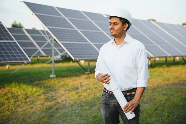 Portrait of Young indian male engineer standing near solar panels, with clear blue sky background, Renewable and clean energy. skill india, copy space.