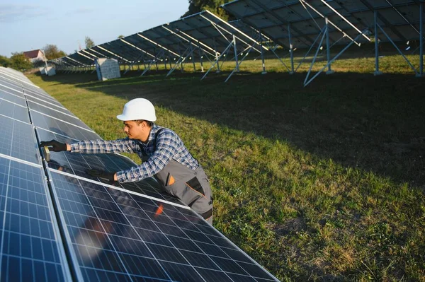 An Indian male worker is working on installing solar panels in a field.