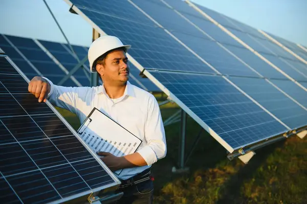 Portrait of a young Indian male engineer or architect at a solar panel farm. The concept of clean energy.
