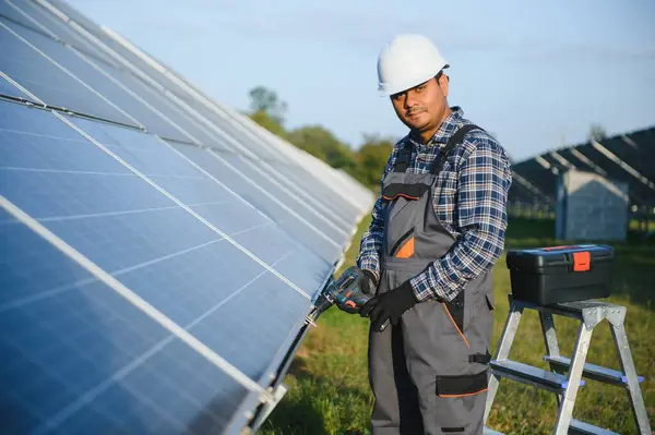 An Indian worker in uniform and with tools works on a solar panel farm.