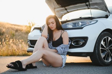 Güzel bir genç kız yolda bozuk bir arabada oturuyor. Yardım almak için yanıp tutuşuyor..