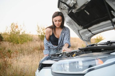 Yazlık şortlu ve gömlekli çekici genç kız bozuk bir arabayı tamir ediyor. Güzel bir kadın arabanın kaputunun yanında duruyor.