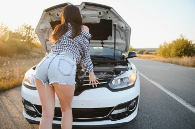 Yazlık şortlu ve gömlekli çekici genç kız bozuk bir arabayı tamir ediyor. Güzel bir kadın arabanın kaputunun yanında duruyor.