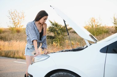 Yazlık şortlu ve gömlekli çekici genç kız bozuk bir arabayı tamir ediyor. Güzel bir kadın arabanın kaputunun yanında duruyor.