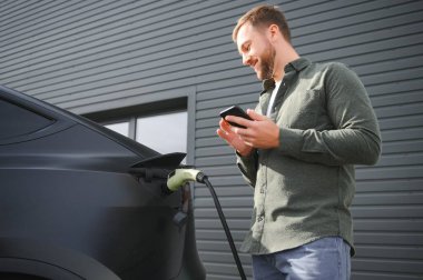 Bir adam modern elektrikli arabasını şarj ediyor. Yeşil enerji kavramı.