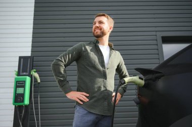 Evin yanında elektrikli araba şarj eden bir adam var..