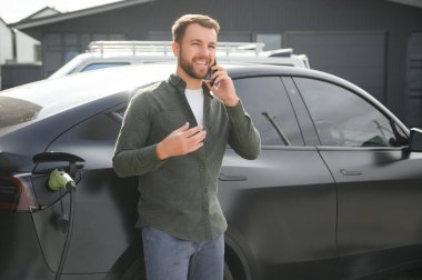 Mutlu adam akıllı telefon kullanıyor ve aracı şarj ediyor..