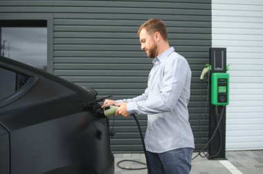 Bir adam elektrikli arabayı şarj eder..